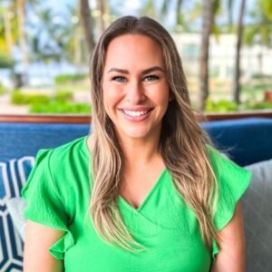 A woman smiling and sitting in a chair wearing a green shirt.