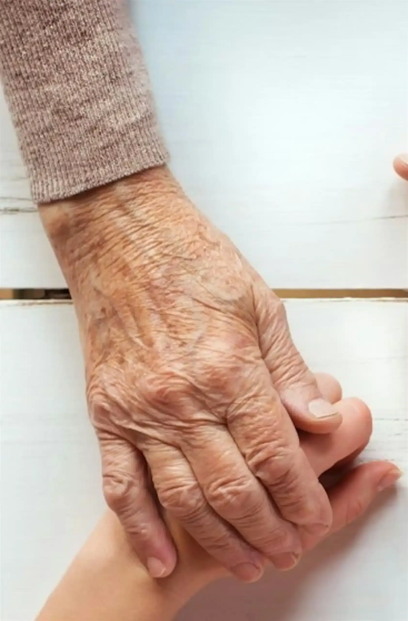 An elderly hand holding a younger hand on a white table